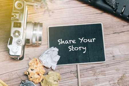 SHARE YOUR STORY word concept with vintage camera, crumple paper,compas and planner book on wooden floor.の写真素材