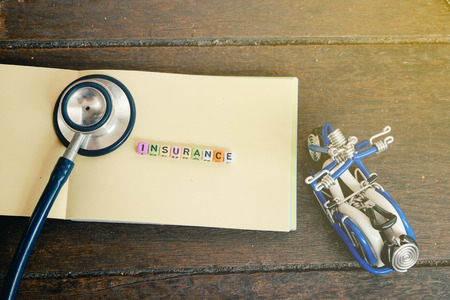 conceptual image with INSURANCE word block on note pad with light effect.handcrafted souvenir and stetoscope on wooden backgroundの写真素材