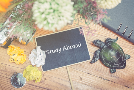 word STUDY ABROAD over top view of vintage camera, crumple paper,compas and planner book layout on wooden floor.の写真素材
