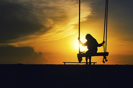 Silhouette of lonely girl with hijab on a swing with magical sunrise background.の写真素材