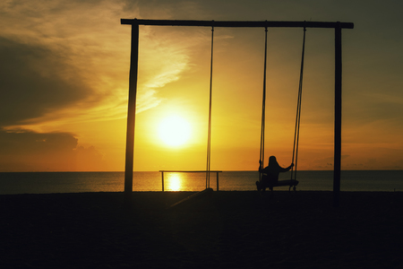 Silhouette of lonely girl with hijab on a swing with magical sunrise background.の写真素材