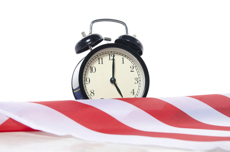 Vintage alarm clock behind white and red stripe flag ideal for concept of measuring passing time,  deadlines and time managementの写真素材