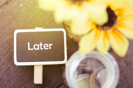 procrastination and urgency concept with word Later on wooden signage, artificial plant and coin in jar. wooden background with light effectの写真素材