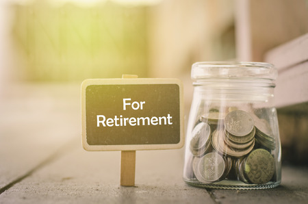 concept image,word RETIREMENT on wooden signage and coin in jar .fade color effect wooden background with light effectの写真素材