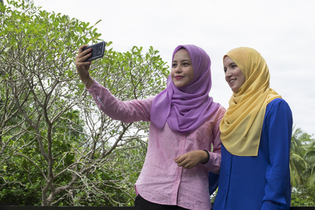 Happy beautiful muslimah having fun, spend time together and selfie at the city parkの写真素材