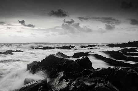 black and white image of seashore and wave hitting rock on the beachの写真素材