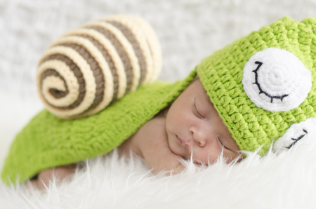 Portrait of sweet newborn baby in knitted snail costume sleeping on white blanket.selective focus shotの写真素材
