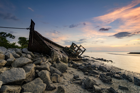blurred and selective focus silhouette image of abandon shipwrecked on rocky shoreline. dark cloud and soft on waterの写真素材