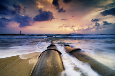 Beautiful white wave flow hitting the sandy beach over dark cloud backgroundの写真素材