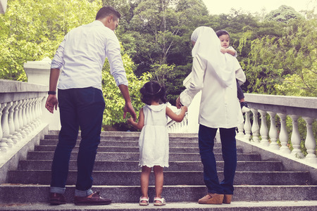 happy family holding hand and walking upstairs together at public park under bright sunny dayの写真素材
