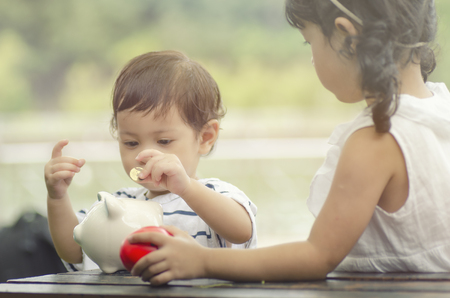 saving concept, two little kids putting coin into piggy bank for their futureの写真素材