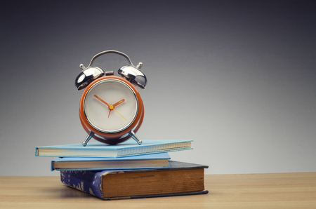 retro alarm clock on stack of book over dark background for education and time management success concept.の写真素材