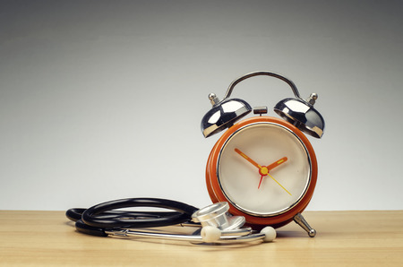 health and medical concept, retro alarm clock and stethoscope on wooden desk over gradient effect backgroundの写真素材