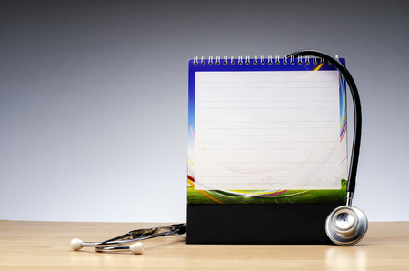health and medical concept, calendar notepad and stethoscope on wooden desk over gradient effect backgroundの写真素材