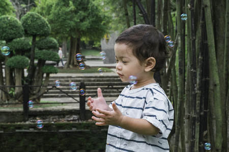 young kid playing with bubble under bright sunny day at public parkの写真素材