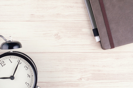 flat lay working desk with alarm clock and diary over wooden background. copy space for textの写真素材