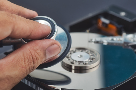 hand holding stethoscope for diagnose old dusty disassembled hard drive from the computer over dark...