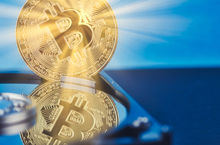 Virtual Cryptocurrency and Blockchain Technology concept, golden bitcoin on dismantle hard disk over gently lit dark background and light rayの写真素材