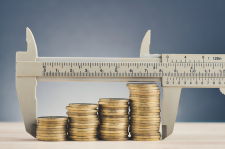 financial crisis and saving money concept,vernier caliper and stacking coins on wooden desk over beautiful reverberation gradient backgroundの写真素材