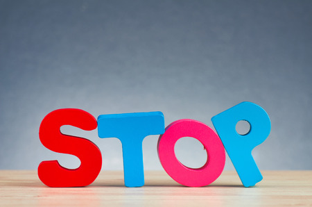 The word STOP spelled using wooden alphabet on desk over  gently lit dark background for banned conceptの写真素材