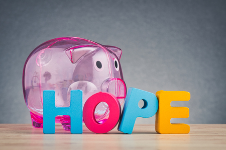 financial crisis concept, HOPE word made from wooden letter and piggy bank on desk over gently lit dark backgroundの写真素材