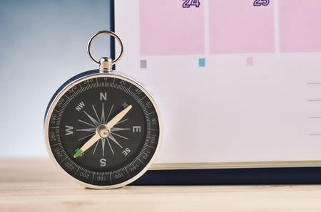 Time Planning and direction concept,  compas and calendar on wooden desk over gently lit dark backgroundの写真素材
