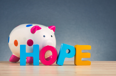 financial crisis concept, HOPE word made from wooden letter and piggy bank on desk over gently lit dark backgroundの写真素材