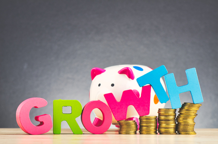 Business success concept, piggy bank, stacking coins and word GROWTH on wooden desk over beautiful reverberation gradient backgroundの写真素材