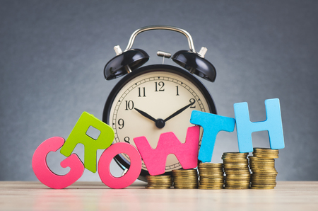 Business success concept, alarm clock, stacking coins and word GROWTH on wooden desk over beautiful reverberation gradient backgroundの写真素材
