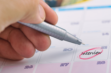 Time planning concept,  cropped hand and yellow sticky paper with word INTERVIEW on calendarの写真素材
