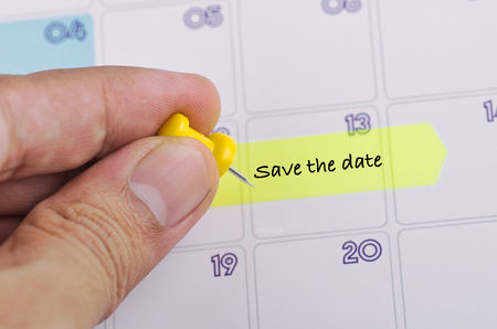 Time planning concept,  cropped hand and yellow sticky paper with word SAVE THE DATE on calendarの写真素材