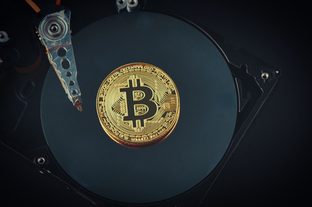 Virtual Cryptocurrency and Blockchain Technology concept, golden bitcoin on dusty dismantle hard disk over dark backgroundの写真素材