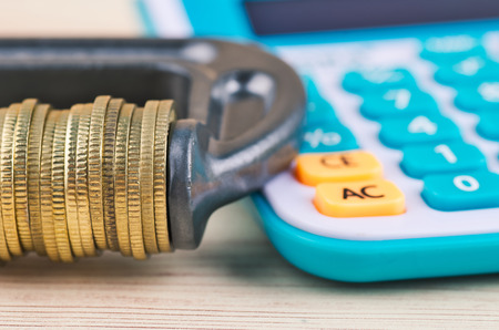 devaluation and financial crisis, calculator and coins squeezed tightly in a G-Clampの写真素材