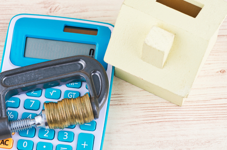 Low budget for home financing, coins squeezed tightly in a G-Clamp on calculatorの写真素材