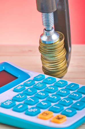 devaluation and financial crisis, calculator and coins squeezed tightly in a G-Clampの写真素材