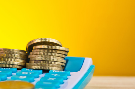 Stacking coins on calculator over beautiful reverberation gradient background for saving business investment conceptの写真素材