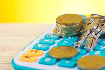 stacking coins and bunch of key on calculator over wooden desk background for home loans conceptの写真素材