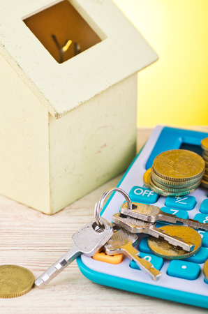 stacking coins and bunch of key on calculator with house replica on wooden desk for home loans conceptの写真素材