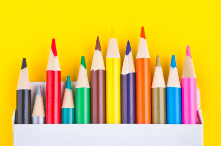 close-up image of colourful pencils in the white box over yellow backgroundの写真素材