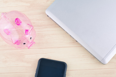 mockup image of laptop, piggybank and hand phone on wooden desk workplaceの写真素材