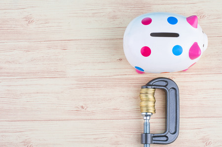 devaluation and financial crisis, piggy bank and coins squeezed tightly in a G-Clamp over wooden backgroundの写真素材