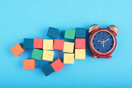 Time management concept, miniature alarm clock and wooden cube on blue background.の写真素材