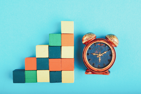 Time management concept, miniature alarm clock and wooden cube on blue background.の写真素材
