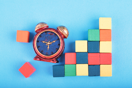 Time management concept, miniature alarm clock and wooden cube on blue background.の写真素材