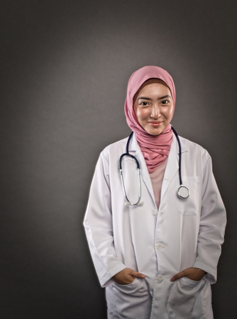 studio shot, closeup portrait of friendly and confident young hijab female doctor over dark backgroundの写真素材