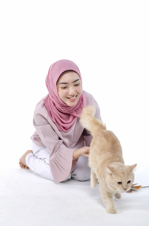 pretty young hijab muslimah play with her cat over white backgroundの写真素材