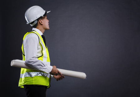 shot from behind of a young architect or engineer holding drawing paper over dark backgroundの写真素材