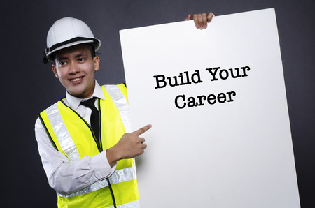 Studio portrait of young engineer or manager with white safety helmet pointing to card with word...
