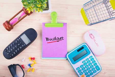 Financial or budget planning concept,top view of notepad with word BUDGET, mobile phone, calculator, and other accessories on wooden backgroundの写真素材