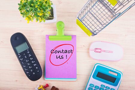 Customer support concept,top view of notepad with word CONTACT US, mobile phone, calculator, and other accessories on wooden backgroundの写真素材